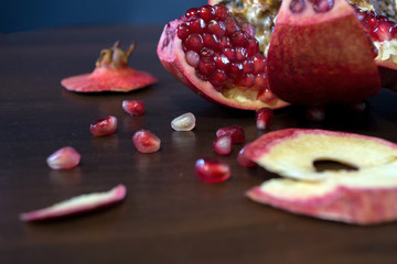 Rotten, spoiled, polished red pomegranate on a wooden table with seeds.