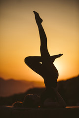 Young woman is practicing yoga on the mountain at sunset. Silhouette of young woman practicing yoga outdoor.