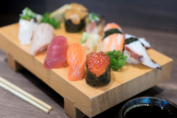 Close-up sushi and sashimi mixed on wooden plate on black wooden table. Japanese food.