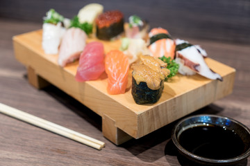 Close-up sushi and sashimi mixed on wooden plate on black wooden table. Japanese food.