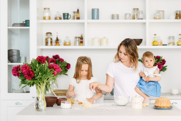 Obraz na płótnie Canvas A young mother with her two children is preparing tasty and healthy food in a large and bright kitchen. woman teaches children how to make dough