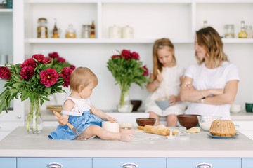 A young mother with her two children is preparing tasty and healthy food in a large and bright kitchen. woman teaches children how to make dough