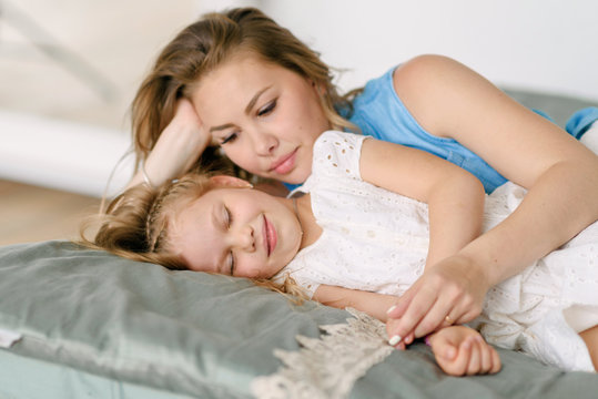 Mom embraces a sick little daughter lying on the bed