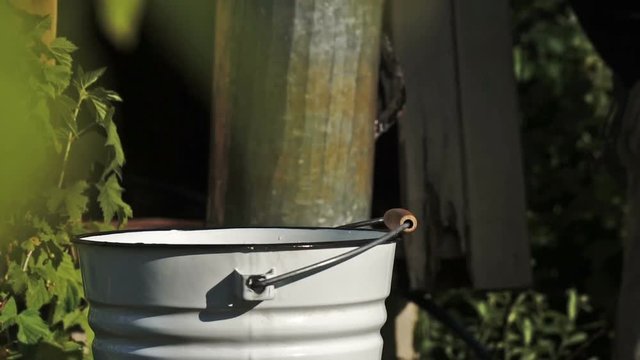 Slow motion shot of a man pouring down into a bucket freshly taken up water from a village draw-well at countryside in summer