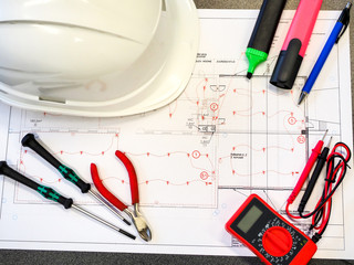 Office table or desk with the project drawings of the security or fire alarm system, a protective helmet, tools, a multimeter and markers.