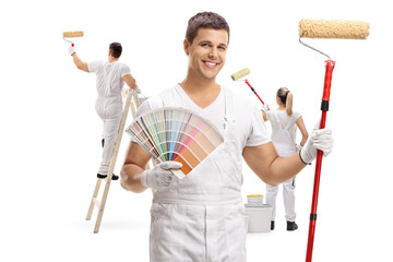 Painter holding a color swatch and a paint roller with two painters painting behind him