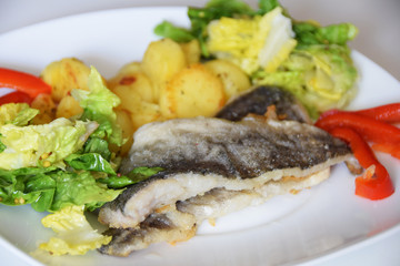 fried cod fish, baked potatoes in a pan, green lettuce with spices,