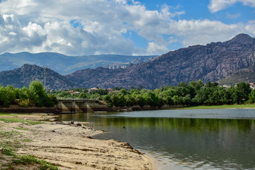 Fototapeta na wymiar View of the reservoir of Manzanares El Real where you can see a bridge and in the background the great mountains of La Pedriza. Photograph taken at Manzanares El Real in Madrid, Spain.