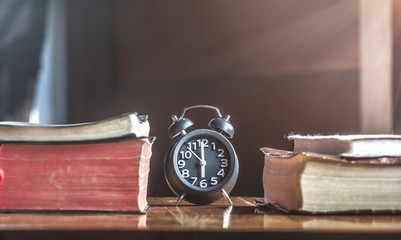 Place the clock with many holy bible on wood table.morning light