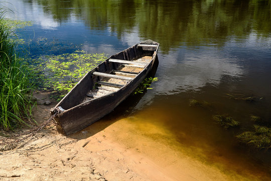 Old rowing boat tied with chain and padlock at green summer bank at noon on Neman river in Grodno Belarus
