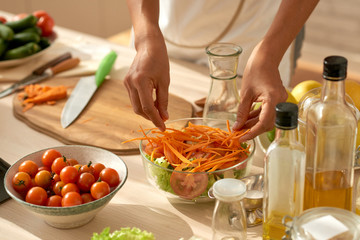 Talented female food blogger putting finishing touches on healthy vegetable salad while standing at kitchen table