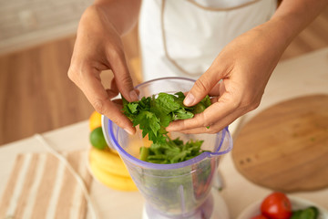 Close-up shot of unrecognizable woman putting mint into blender while preparing healthy smoothie at home