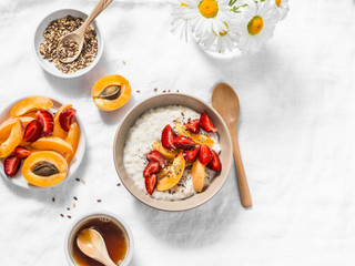 Coconut milk oatmeal porridge with strawberries, apricots, honey and flax seeds. Delicious healthy breakfast on a light background, top view. Flat lay