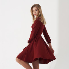 Fototapeta premium Young blonde woman in cherry red dress standing and posing on white background. Female with long straight hair.