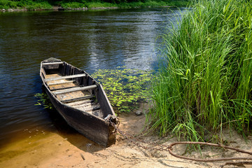 Old wooden rowing boat tied with chain and padlock at green summer bank on Neman river in Grodno...