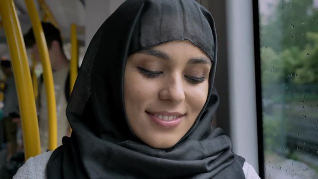 Young beautiful muslim woman in hijab is watching at camera in bus, transport concept, urban concept, weather concept, dreaming concept