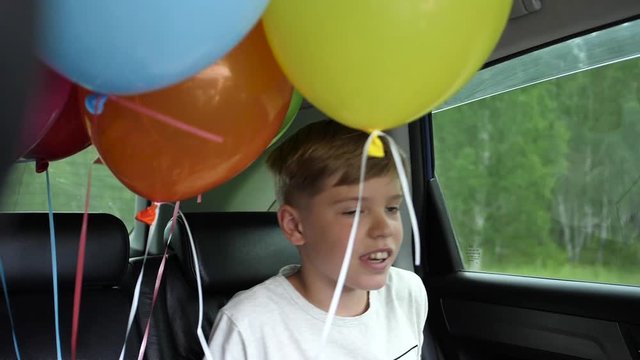 Happy child riding in a car. Festive mood, smile, laughter. Balloons in the car