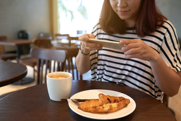Smiling woman wearing striped T-shirt sitting at cafe table and taking picture of appetizing...