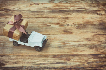toy car carries wrapped gift box, on wooden table