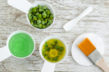 Three white scoops with aloe vera gel mask, wild chamomile oil and pineappleweed flowers for natural skin care and medicinal purposes. Homemade cosmetics and phytotherapy concept. Top view, copy space