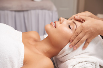 Fototapeta na wymiar Calm female taking pleasure in relaxing massage on her face in spa salon