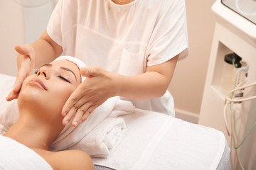 Obraz na płótnie Canvas Young beauty specialist touching cheeks of client to calm skin down after skincare procedure