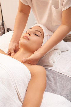 Cosmetician making neck massage while her client relaxing on soft towels