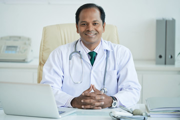 Portrait of smiling Indian male doctor sitting at his workplace