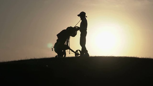 Silhouette of boy golfer with golf bag at sunset