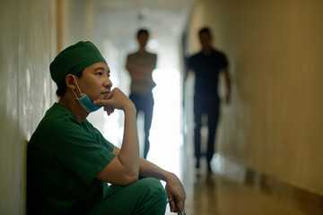 Pensive male surgeon sitting at corridor after operation