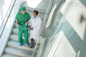 Doctor and surgeon standing on staircase and discussing method of treatment together