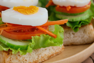 Open faced sandwich with toast lettuce tomato carrot cucumber and boil egg on wooden plate in close up view. Delicious breakfast for family served on wood table. Homemade and healthy food concept.