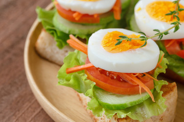 Open faced sandwich with toast lettuce tomato carrot cucumber and boil egg on wooden plate in close up view. Delicious breakfast for family served on wood table. Homemade and healthy food concept.