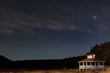 Stary night sky in the mountains with a little white and brown gazebo.