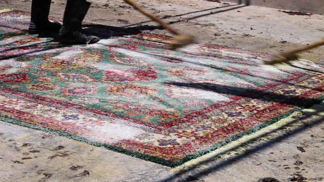 A medium shot of a carpet being cleaned by two people. The carpets are made in Kabul.
