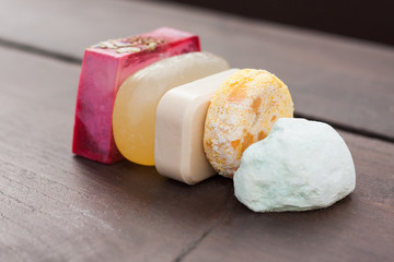 A colourful selection of stacked natural soap, shower gel, bath bomb and shampoo bars on a dark wooden table. For a zero waste, plastic free bathroom and home.