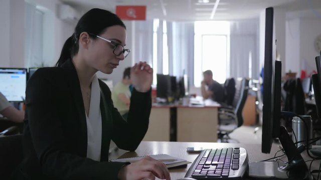 business girl with glasses works in the office at the computer and uses mobile phone