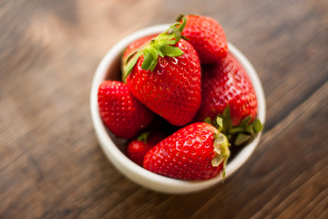 Fresh and sweet ripe red strawberries from Spain on a dark wooden table outdoors. Served as a healthy snack or dessert in a small white ceramic bowl.