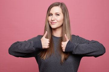 Photo of attractive self assured young female model keeps thumb raised, shows like gesture,...