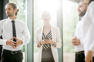Business people strictly dressed in white having a conversation standing together at the office hall with sunlight indoors