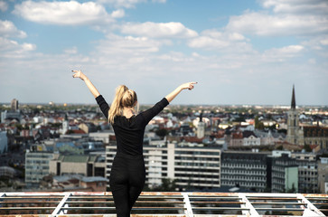 Fototapeta na wymiar Young woman on rooftop with raised hands