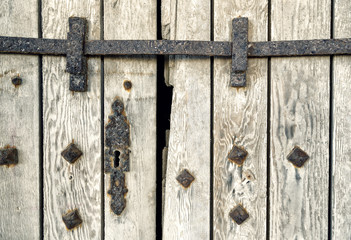 Rusty keyhole and latch on the wooden gate with bolts of a medieval castle