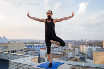 Fototapeta na wymiar Tree Pose(Vrksasana) A middle-aged man is engaged in yoga on the roof.