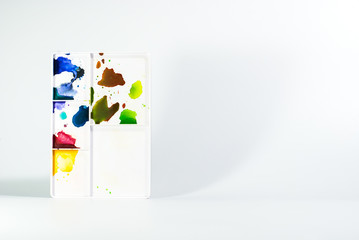 White plastic watercolor mixing tray standing on white background, there are some color stains on it, painting hobby