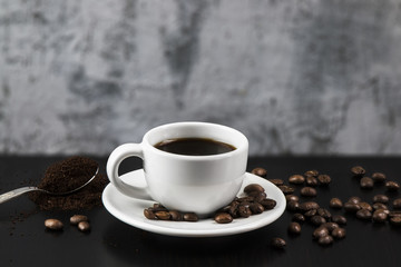 Still life with white cup with delicious coffee and coffee beans on dark background