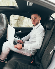 Confident young businessman working on his laptop while sitting in the car