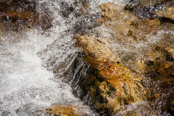 Close-up streams of water between mountain stones. Beautiful mountain river stream with fast flowing water and rocks. Flowing water in beautiful landscape. Picturesque rapids on the river.