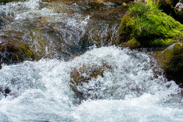 Water in a mountain stream breaking on rocks and stones creating a white foam