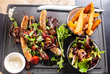 Delicious Hot Grilled Sausages, Baked Potatoes, White Sauce and Fresh Vegetables  Salad on Black Salver, View From Above.