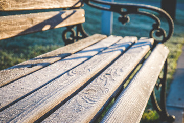 Wooden bench with forged cast iron handles and planks covered with sparkling hoar frost. Shallow...